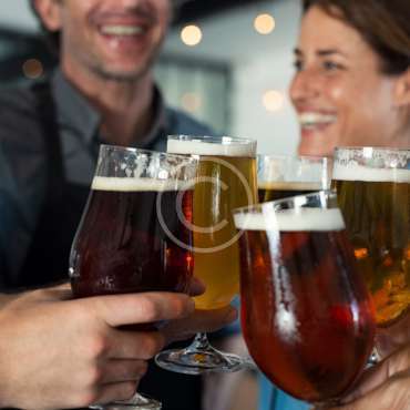 Happy friends clinking glasses of tap beer. Closeup hands of mature men and women toasting with draught beer. Hands holding beer for raising a toast to celebrate. People cheering to success with pints of beer.